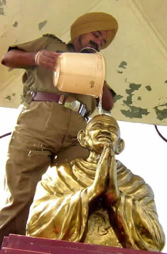 Indų policininkas pila vandenį ant Mahatma Gandhi statulos