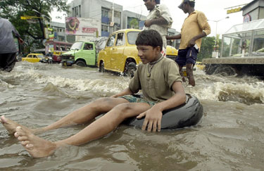 Berniukas plaukia ant pripučiamos padangos potvynio užtvindyta Kalkutos gatve.