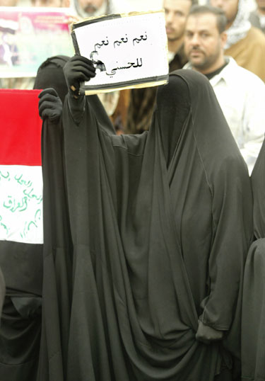 Šiitų dvasininką Mahmudą al-Hassani palaikanti musulmonė moteris protestuoja su plakatu, kuriame parašyta “Taip, taip, taip al-Hassanui”.