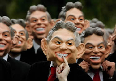 žmonės pozuoja fotografams užsidėję kaukes su Tony Blairo atvaizdu